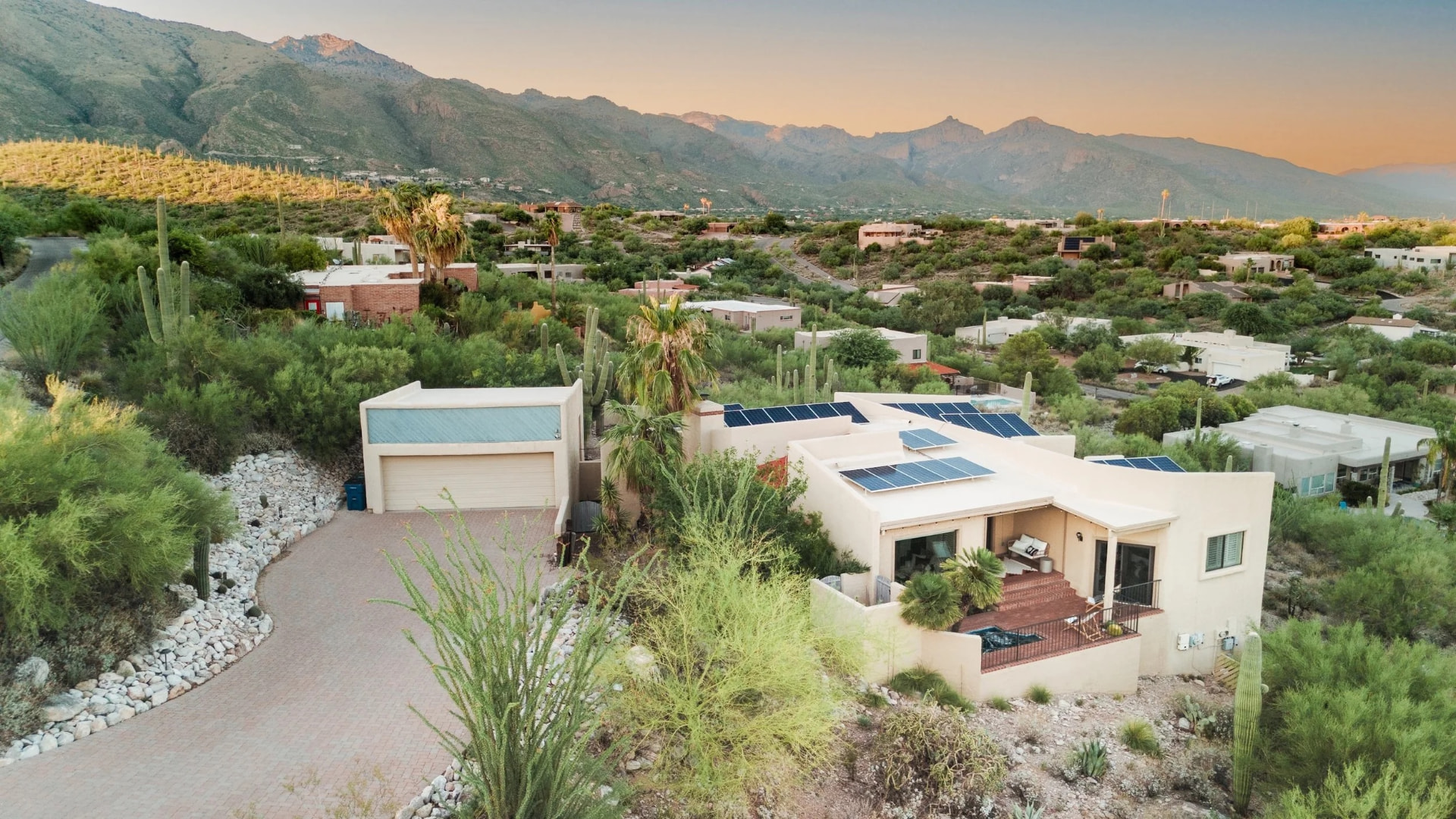 Casa Saguaro, a tan southwestern home with solar panels set against desert mountains at sunset